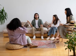 Menschen sitzen in einer gemütlichen Runde auf flachen Sofas und sprechen.